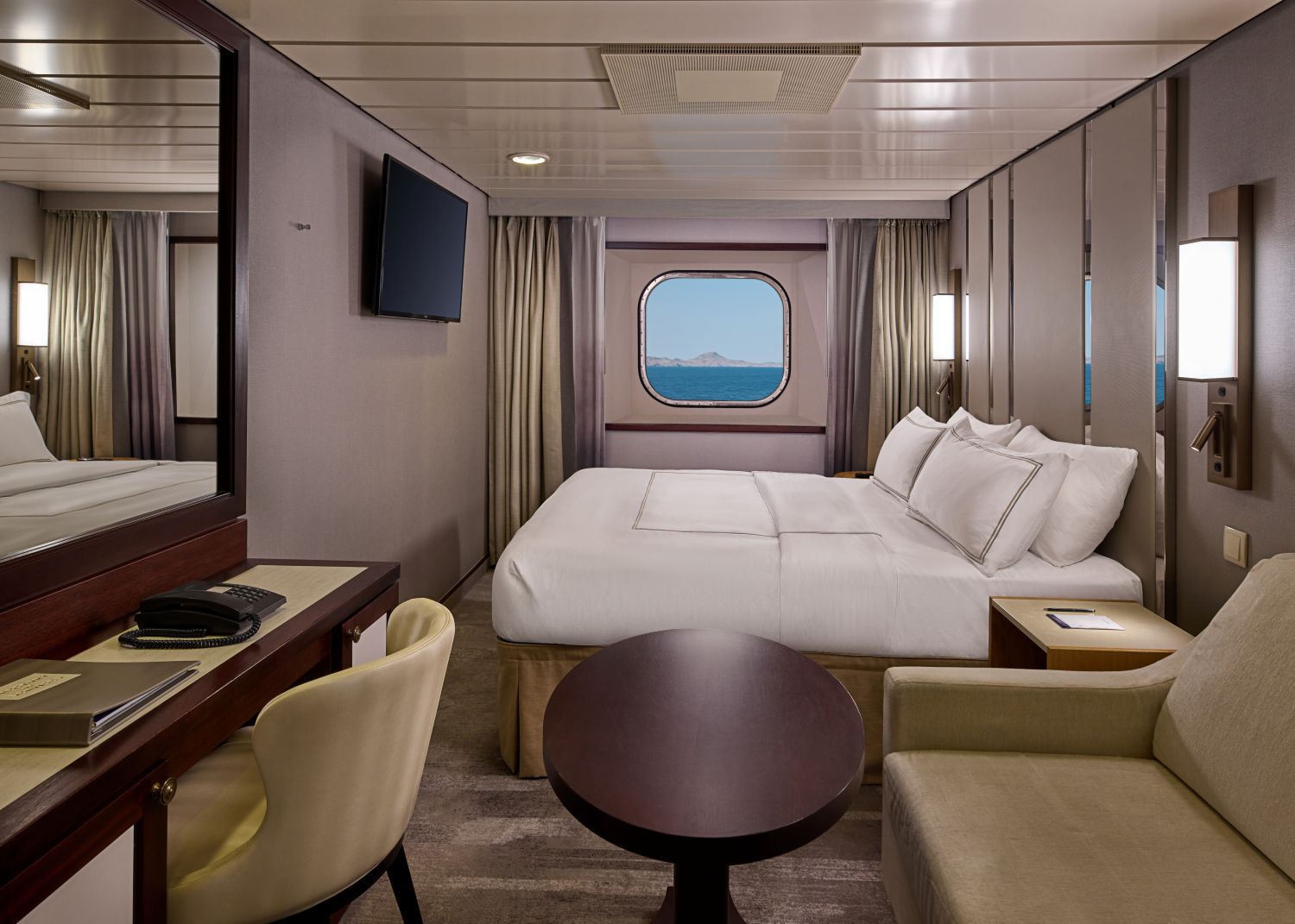 stateroom featuring queen bed, sitting area, desk, and window